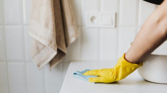 Close-up of a person wearing yellow gloves wiping a bathroom counter with a cloth.