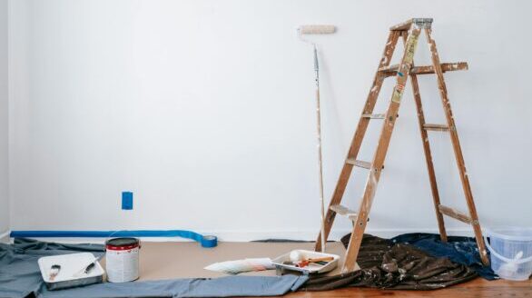 A room prepared for renovation with a ladder, paint supplies, and drop cloth.